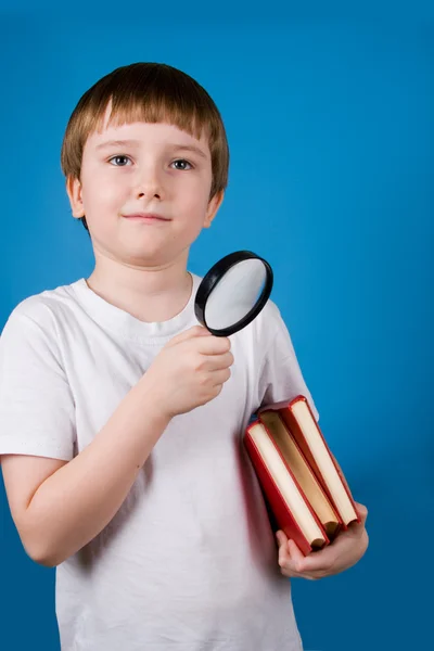 Boy with magnifying glassa and pile of books — Stock Photo, Image