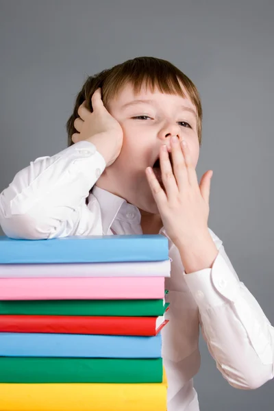 Boy with a pile of books yawns — Stock Photo, Image