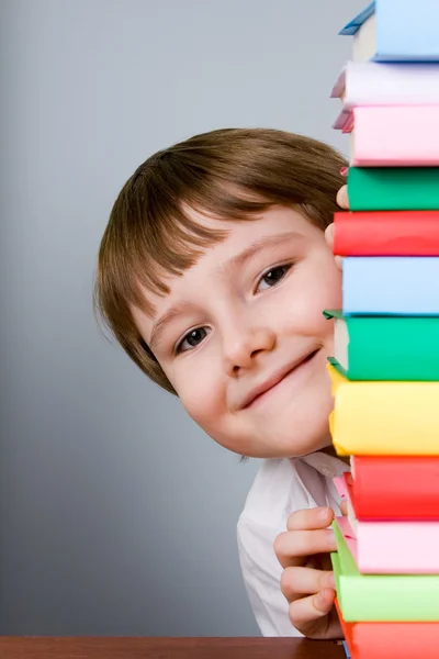 Boy looks out from a stack of books — Stock Photo, Image