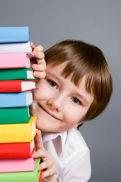 Jongen kijkt uit van een stapel boeken — Stockfoto