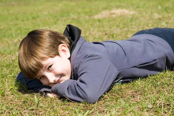 เด็กชายที่มีความสุขนอนบนทุ่งหญ้าฤดูใบไม้ผลิ — ภาพถ่ายสต็อก