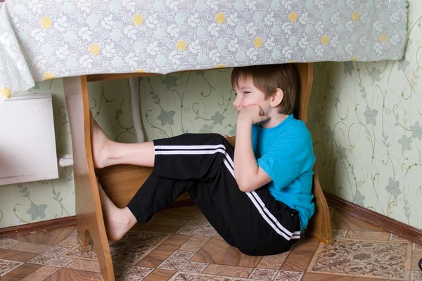 Rapaz senta-se debaixo de uma mesa — Fotografia de Stock