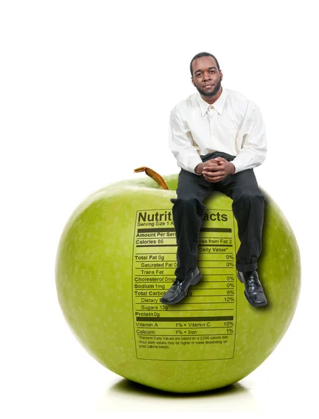Человек сидит на зеленом яблоке с этикеткой питания — стоковое фото