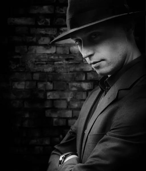 Чоловік з капелюхом стоїть на фоні темної цегляної стіни — стокове фото