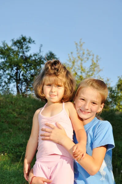 Two little girls standing together in the park, one holds another — Stock Photo, Image