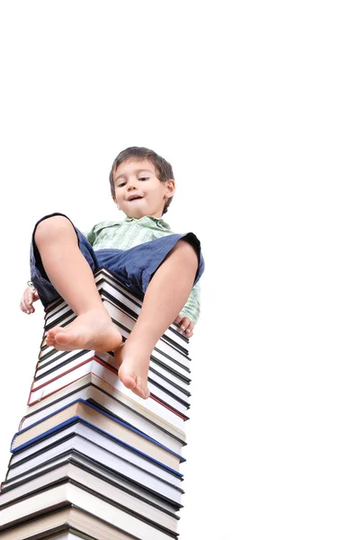 Bonito menino sentado em uma grande pilha de livros — Fotografia de Stock