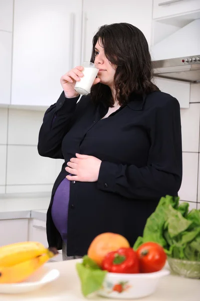 Gravid kvinna dricker mjölk i köket — Stockfoto