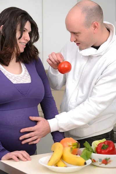 Retrato de um homem bonito dando batata para sua esposa grávida na cozinha — Fotografia de Stock