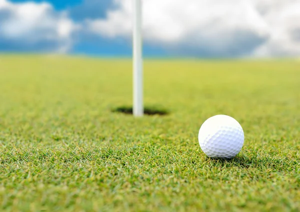 Golf ball op gat op grasveld Stockfoto