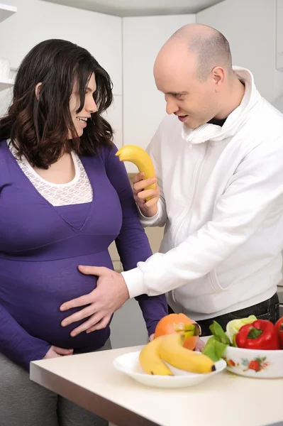 Porträt eines gutaussehenden Mannes, der seiner schwangeren Frau in der Küche Gemüse gibt Stockbild