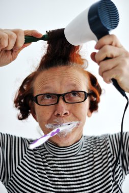 Senior woman brushing teeth and drying hair clipart