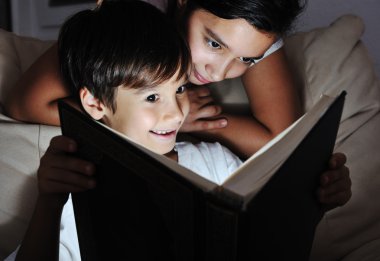 Boy and girl reading light book at night, children concept clipart