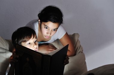 Brother and sister reading light book at night clipart