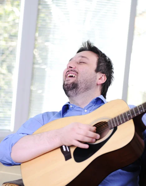 Человек играет на гитаре и поет в помещении на диване — стоковое фото