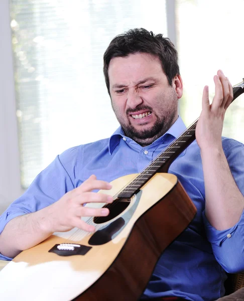 Чоловік грає на гітарі і співає в приміщенні на дивані — стокове фото
