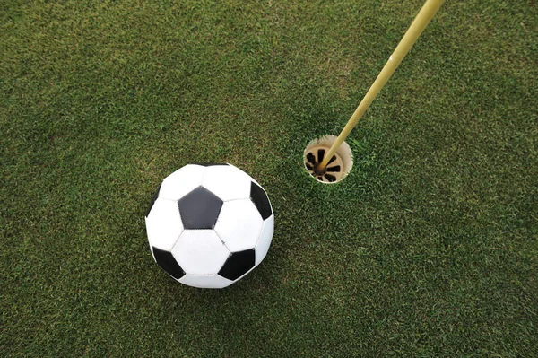 Football big ball at golf field hole — Stock Photo, Image