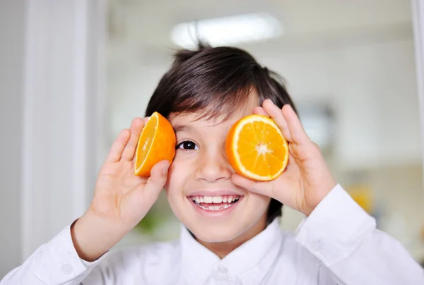 Little boy playing with orange slices on eyes as glasses — Stock Photo, Image