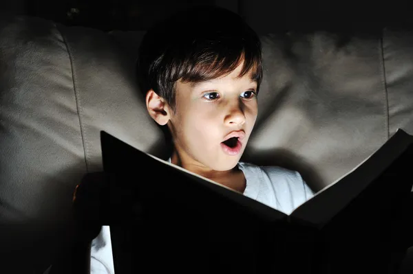 Criança chocada lendo livro, luz na escuridão — Fotografia de Stock