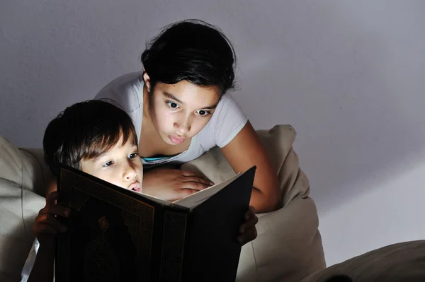 Fratello e sorella leggere libro luce di notte — Foto Stock