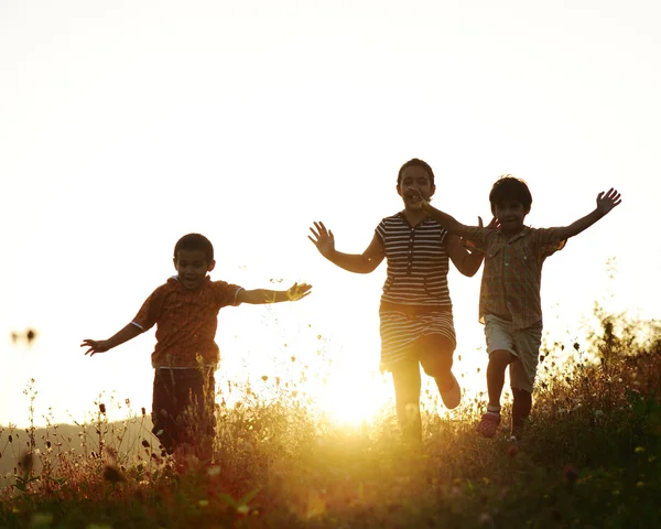 Děti běží na louce při západu slunce — Stock fotografie