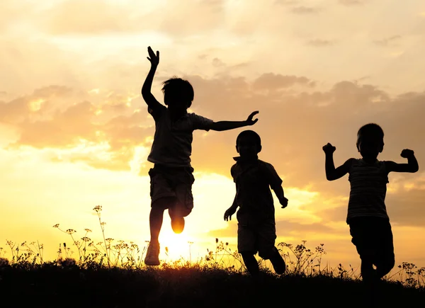 Kinder laufen bei Sonnenuntergang auf Wiese — Stockfoto