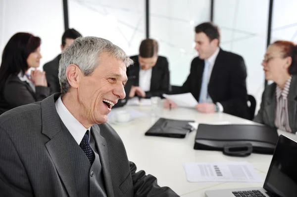 Un uomo d'affari anziano ad una riunione. Gruppo di colleghi sullo sfondo — Foto Stock