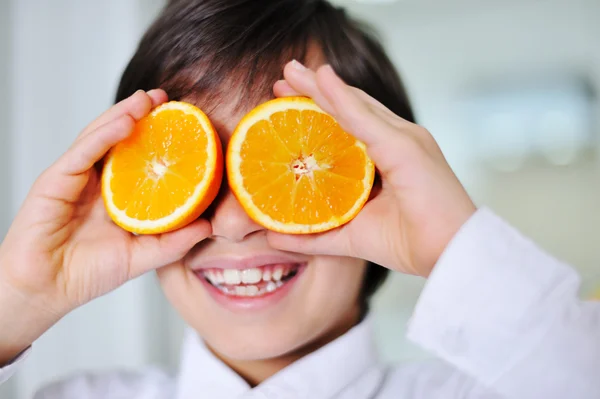 サングラスとして目にオレンジのスライスを保持している小さな男の子 ロイヤリティフリーのストック画像
