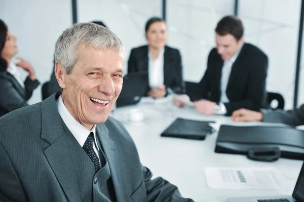 Un uomo d'affari anziano ad una riunione. Gruppo di colleghi sullo sfondo Fotografia Stock