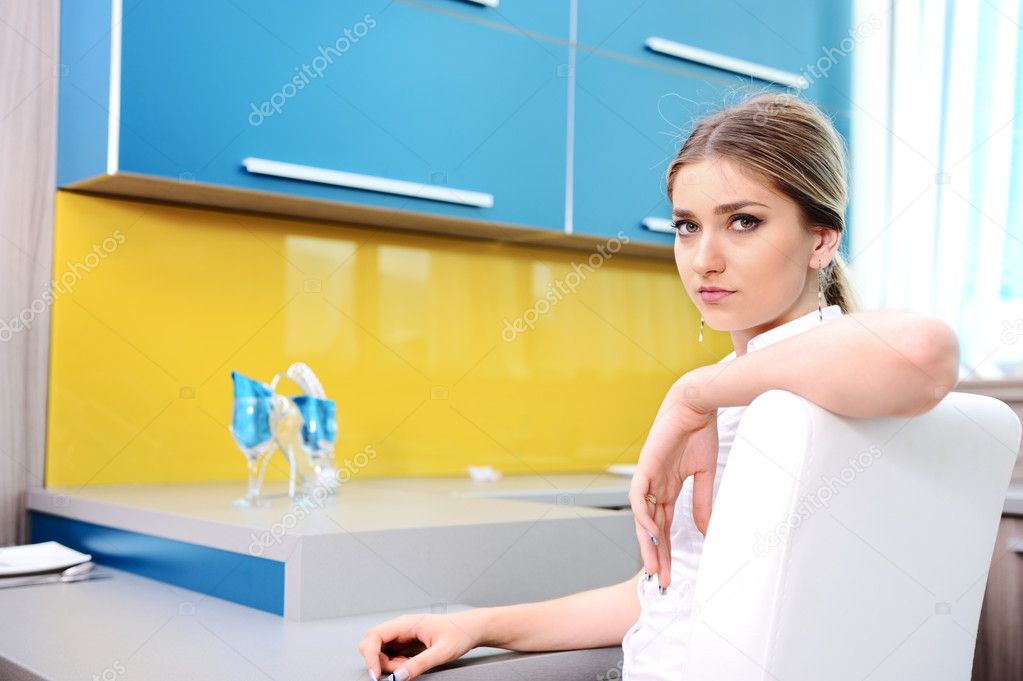 Young beautiful blonde woman in kitchen sitting on chair