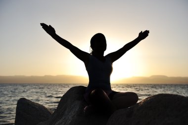 Silhouette of a beatiful female meditating on a rock by the sea clipart