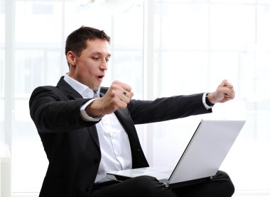 Happy executive raising fists in excitement, in front of laptop clipart