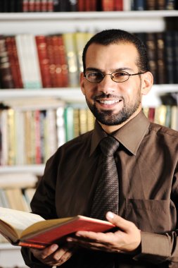 Young man reading book in library clipart