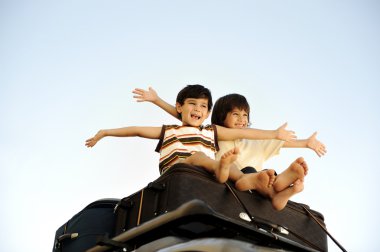 Two little boys traveling on bags, the top of the car clipart