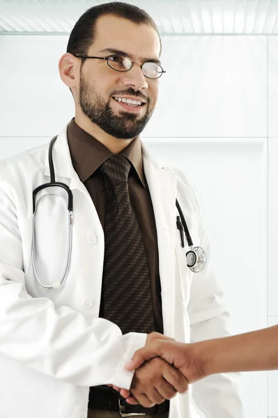 Joven médico adulto estrechando la mano de paciente y sonriente —  Fotos de Stock