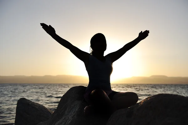 Silhouet van een mooie vrouw mediteren op een rots aan de zee — Stockfoto