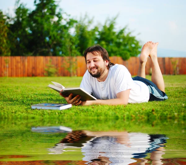 Young happy man on meadow reading — Stock Photo, Image