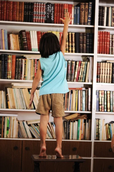 Kid trying to reach a book in the library — Stock Photo, Image