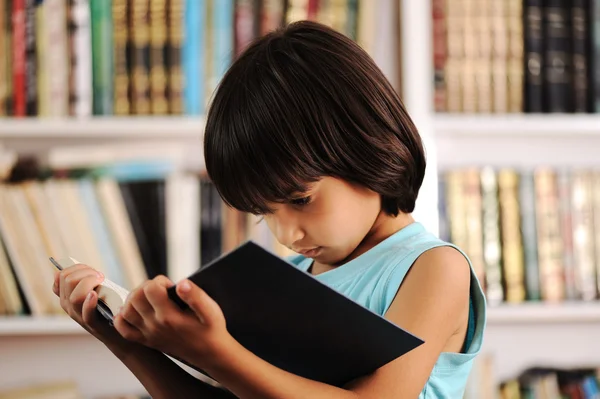 Niño con libro en la biblioteca —  Fotos de Stock