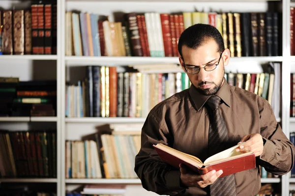 Jovem homem leitura livro na biblioteca — Fotografia de Stock