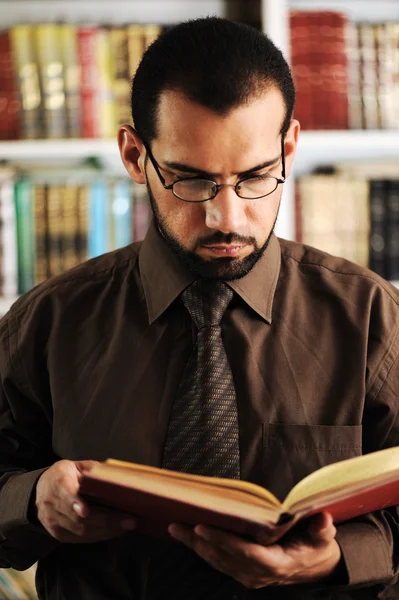 Junger Mann liest Buch in Bibliothek — Stockfoto