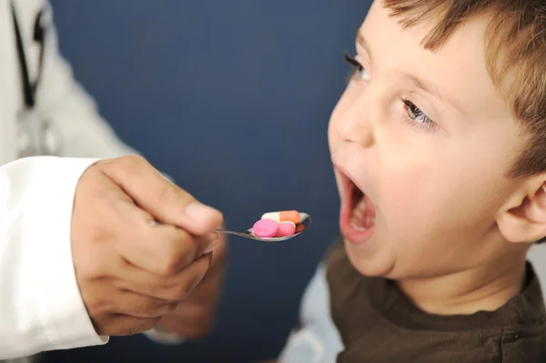 Médico dando uma colher para uma criança cheia de pílulas — Fotografia de Stock