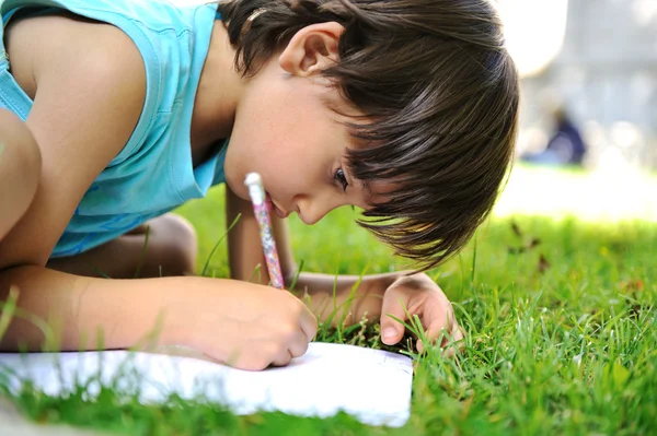 Мальчик на улице на траве пишет — стоковое фото