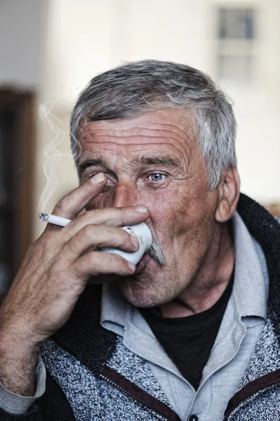 Old man with mustache smoking cigarette and drinking coffee — Stock Photo, Image