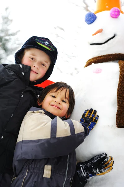 Дети на снегу со снеговиком — стоковое фото