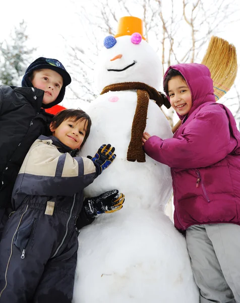 Barn på snö med stor snögubbe — Stockfoto