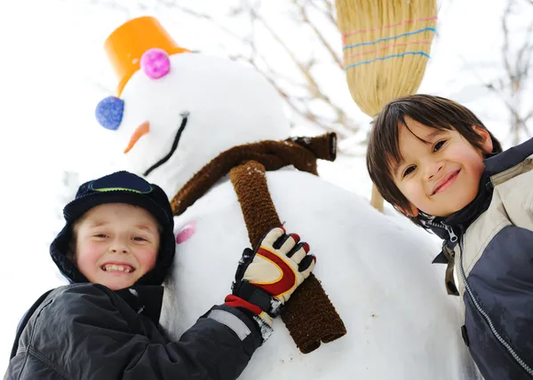 Дети на снегу со снеговиком — стоковое фото