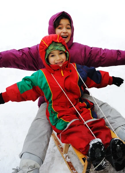 Мальчик и девочка катаются на санках по снегу, счастье для брата и сестры — стоковое фото