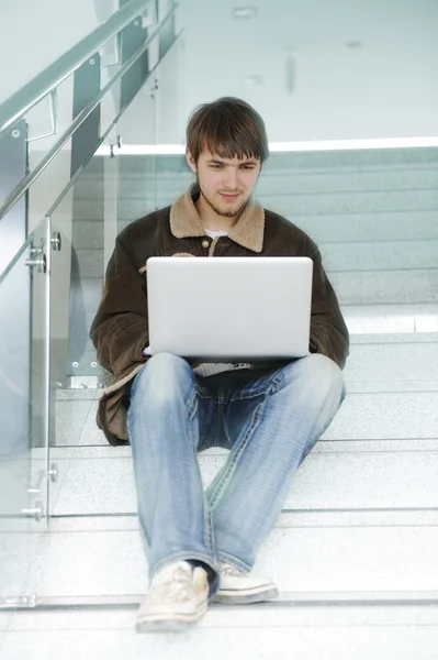 Relajado joven que trabaja en el ordenador portátil, mientras que sittinig interior en el paso del edificio —  Fotos de Stock