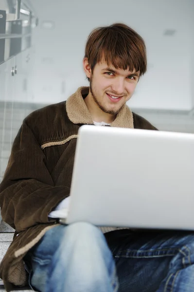 Relajado joven que trabaja en el ordenador portátil, mientras que sittinig interior en el paso del edificio — Foto de Stock