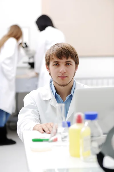 Jovem cientista médico que trabalha em laboratório moderno, pesquisa com tubos e nota — Fotografia de Stock